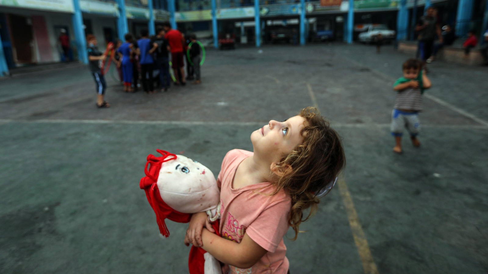 Little girl in Gaza holds a doll and looks up in shelter.