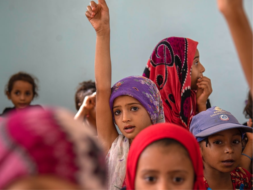 girl raising her hand in her classroom with her classmates