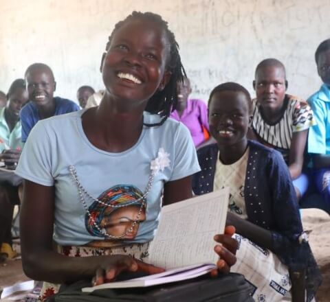 ajak smiling in her classroom holding a notebook