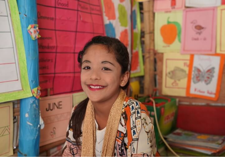 Jannat sitting on her classroom floor smiling at the camera