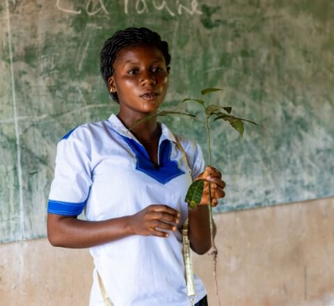 Meda talking in front of her class holding a plant