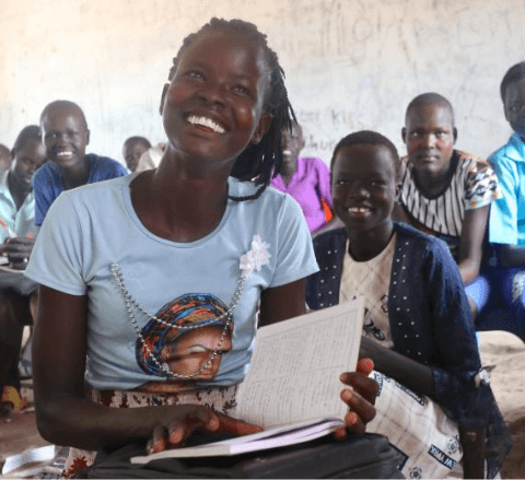 Ajak smiling and holding a workbook at school with her classmates