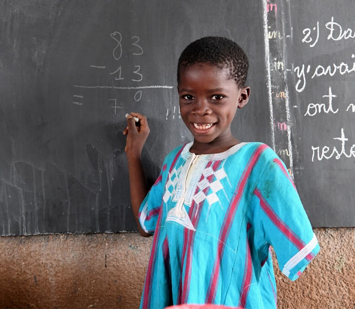 A student with one arm smiling and performing arithmetic on the chalkboard