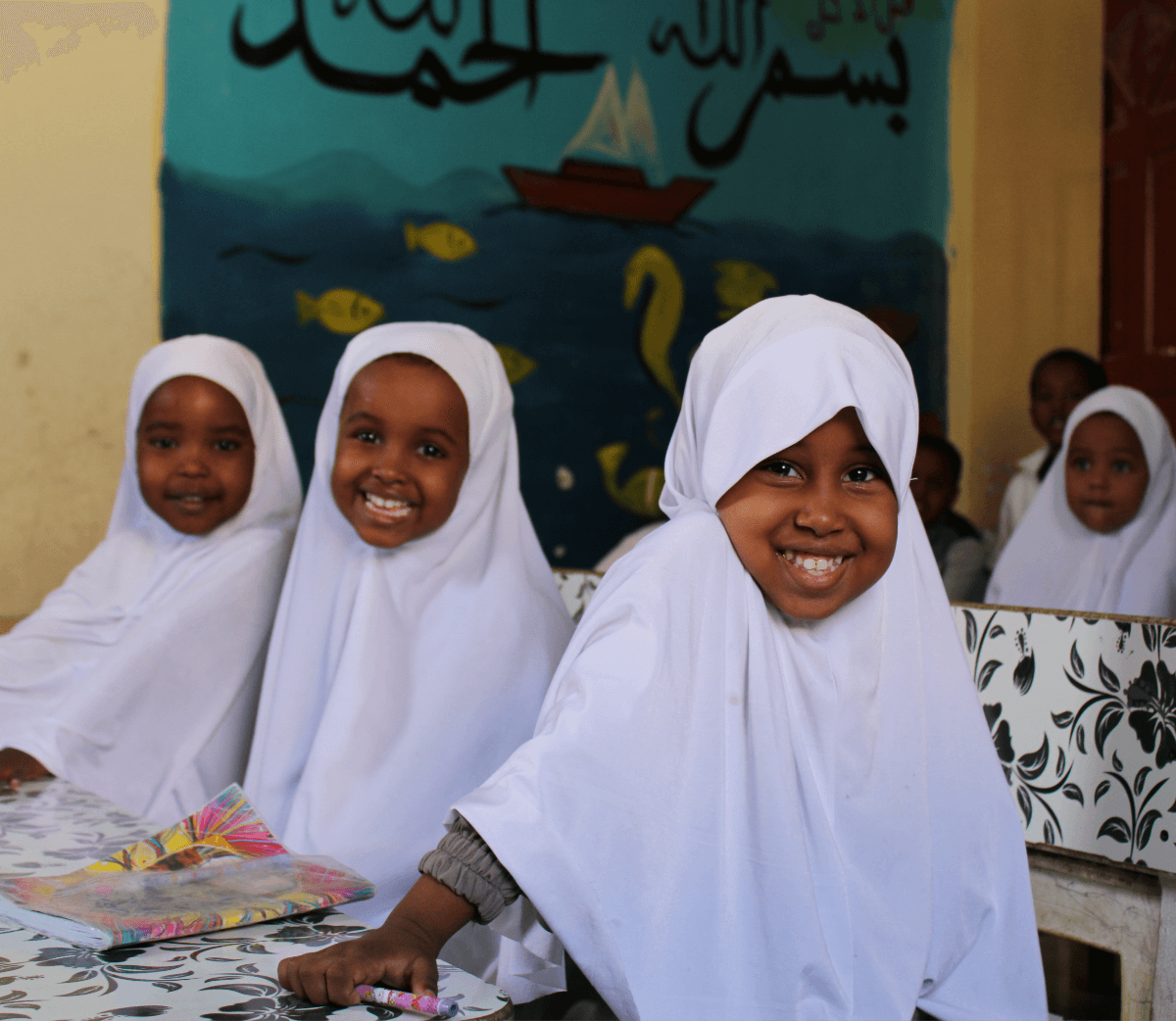 Three students in their classroom wearing white headscarves and smiling