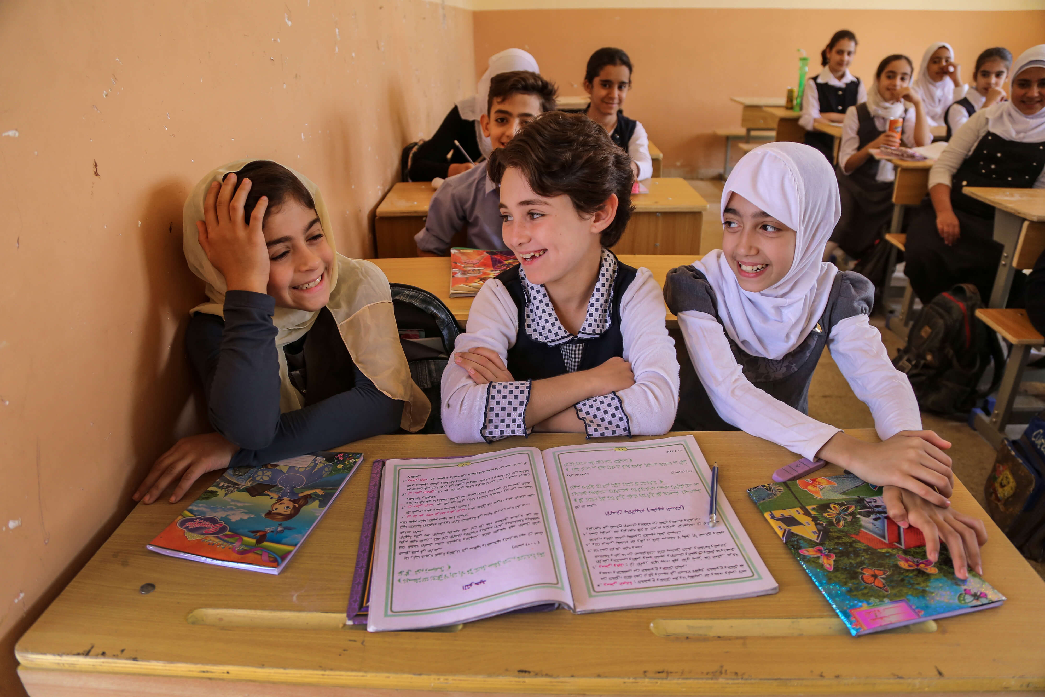girls in their classroom sitting at a table smiling and laughing
