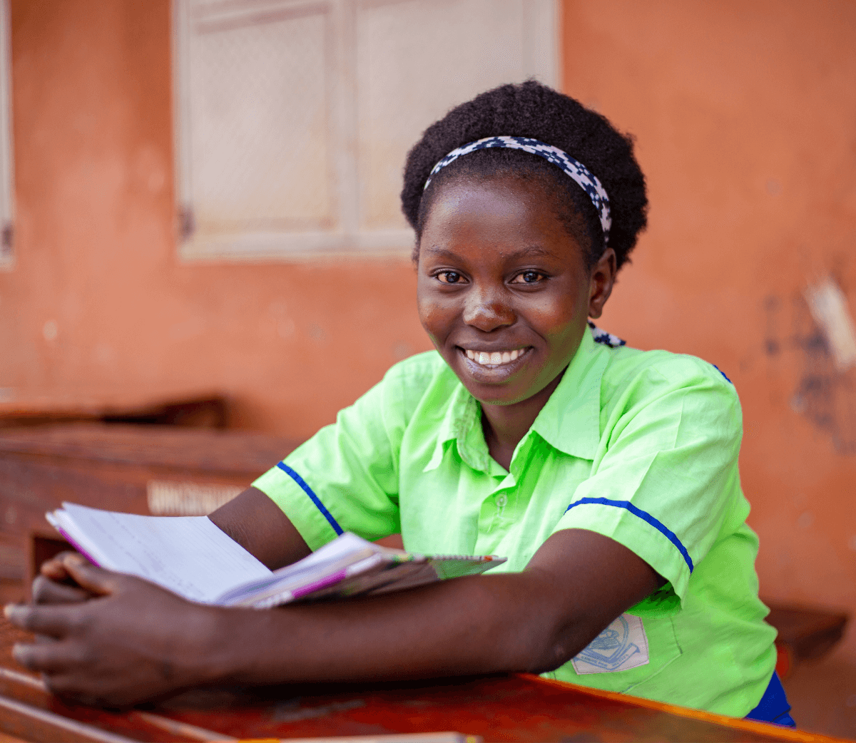 A student in a green shirt holding her notebook and smiling