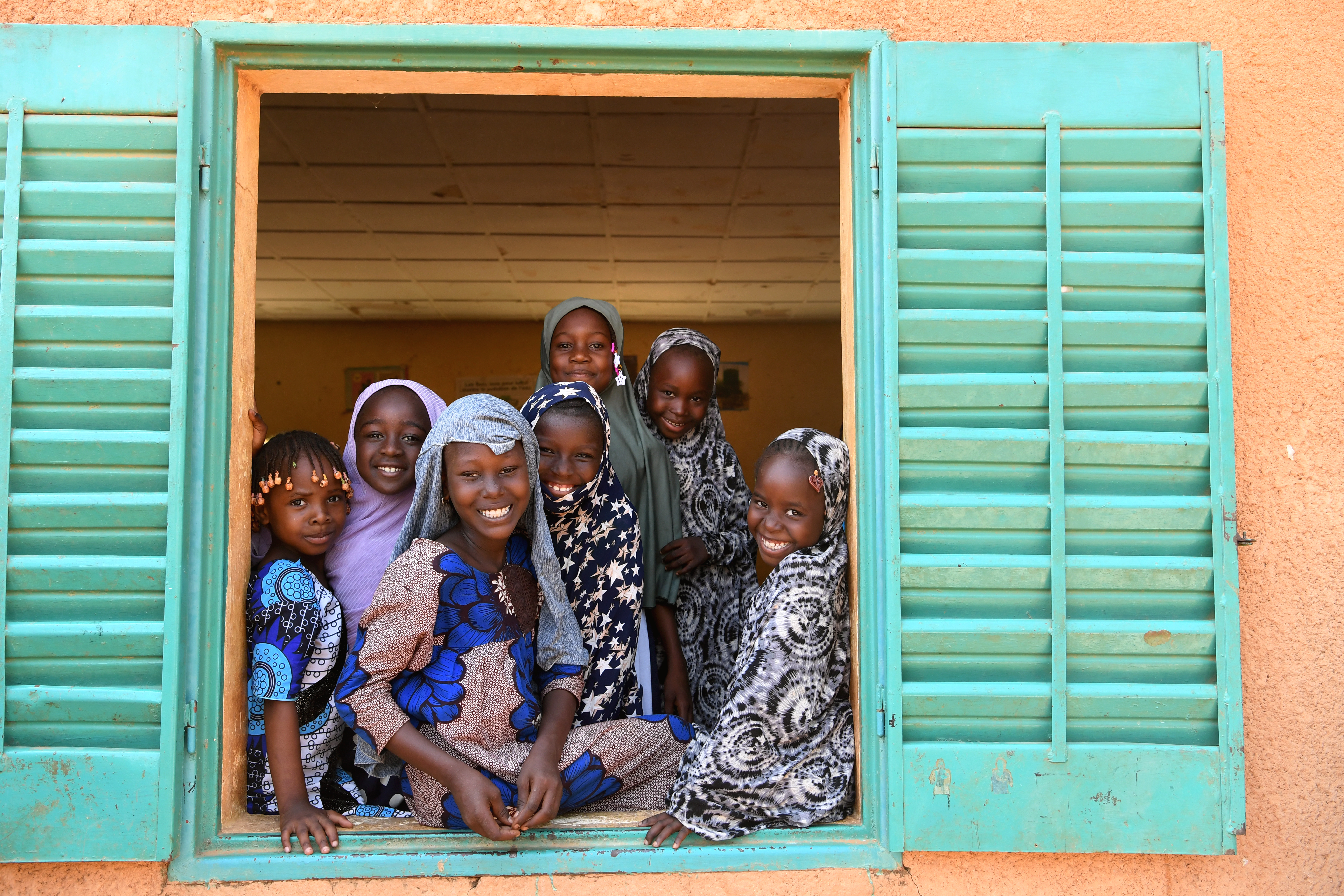 Group of girls in Niger look out a window and smile.