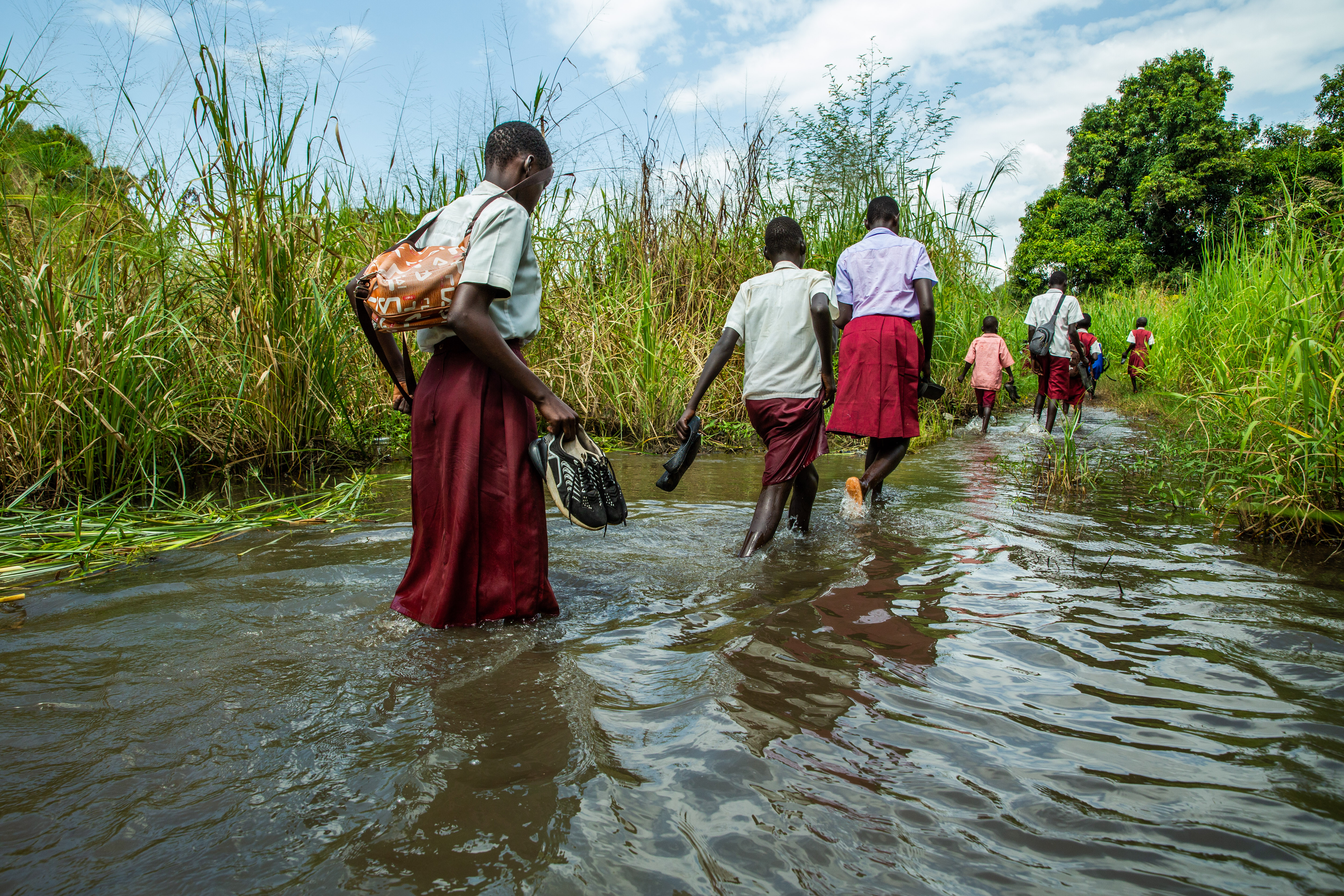 Students in South Sudan walk through flood water.