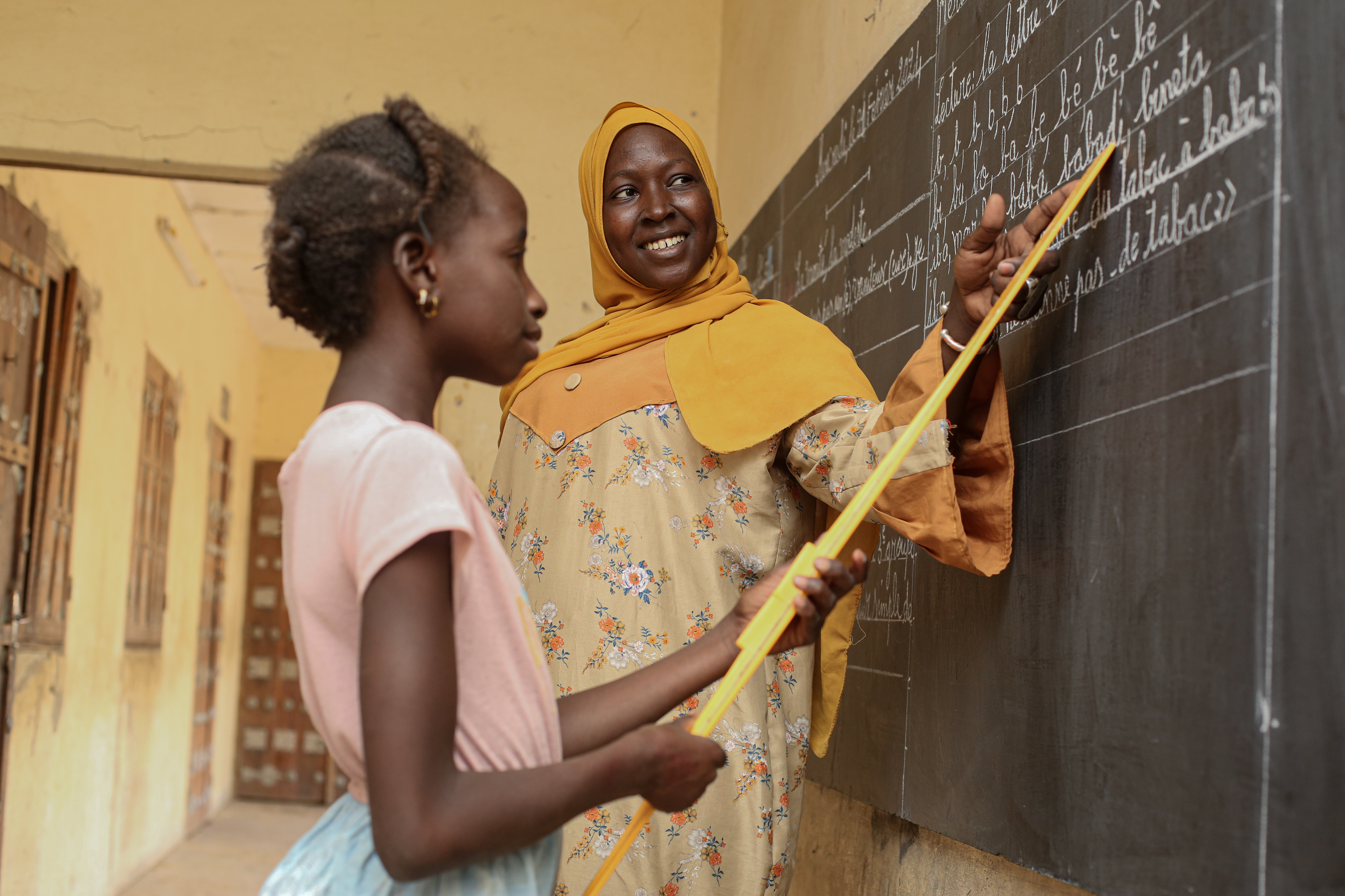 Teacher with student inside a classroom pointing at a blackboard