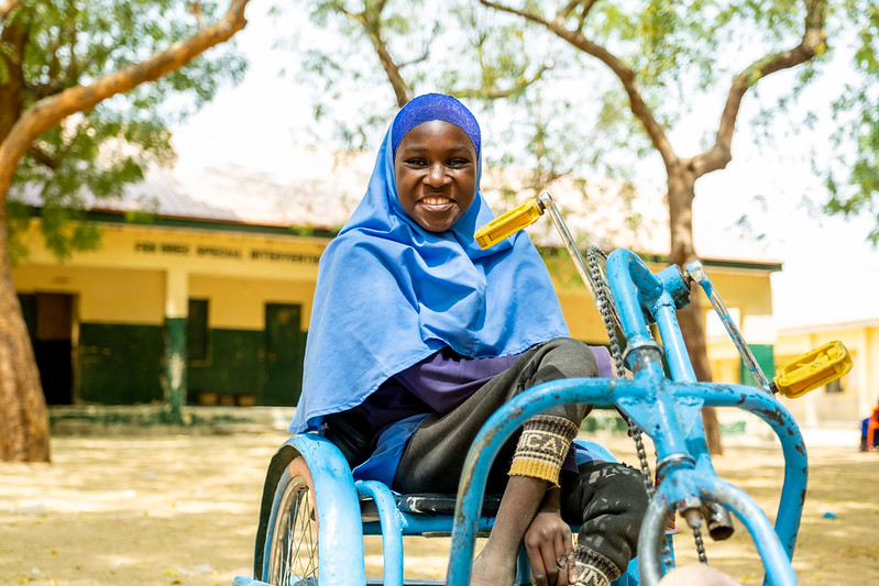 Girl in her wheelchair smiling to the camera outside her classroom