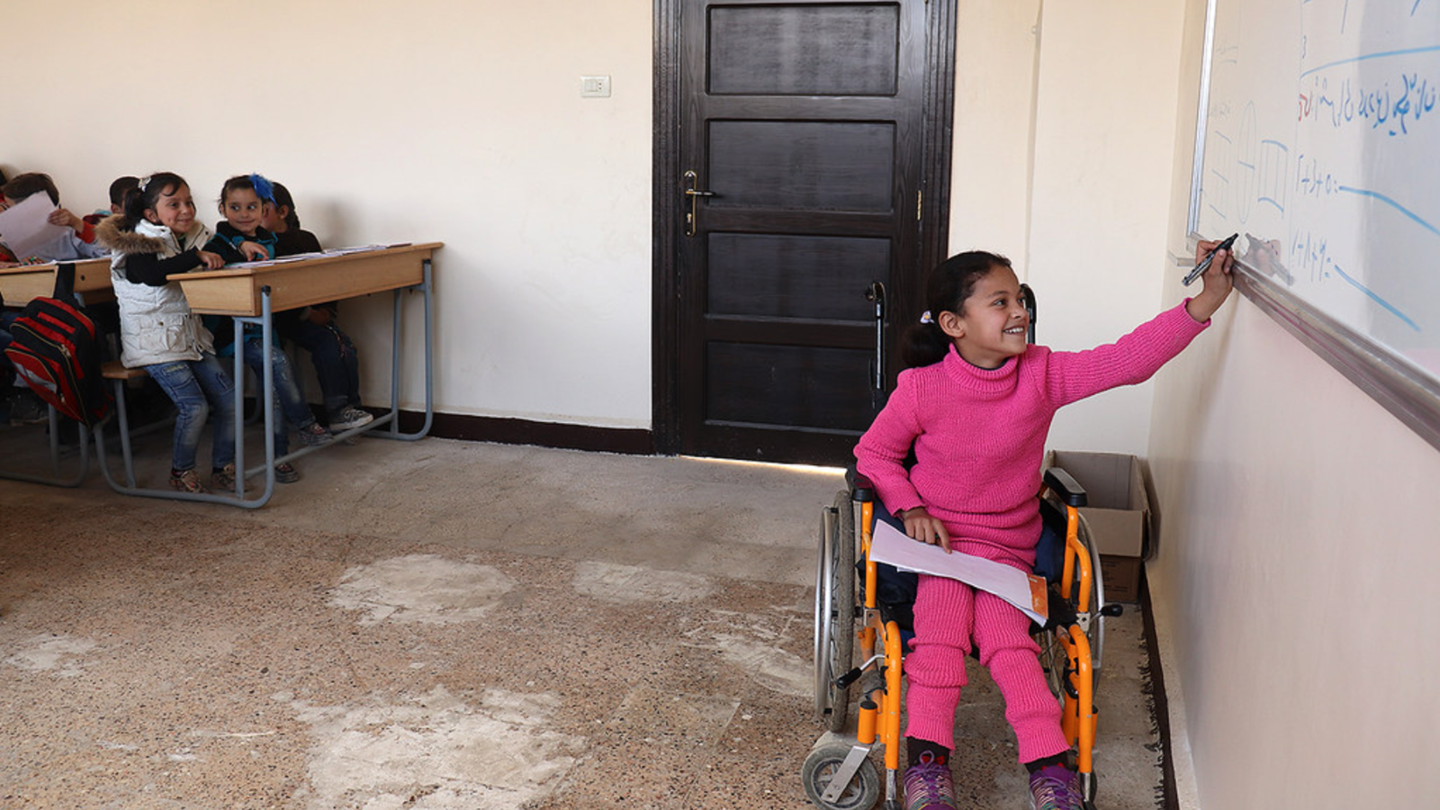 Girl in a wheelchair in Syria writing on the board.