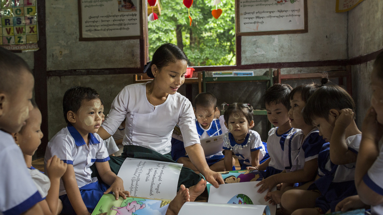 Teacher in Myanmar surrounded by young students.